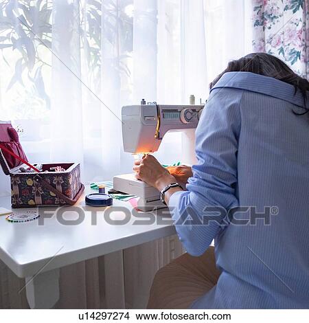 Woman threading sewing machine needle beside window View Large Photo Image Picture - Woman threading sewing machine needle beside window. Fotosearch