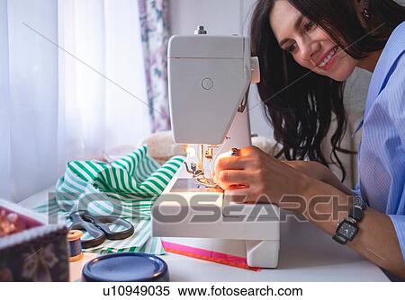 Stock Photography - Woman threading sewing machine needle beside window. Fotosearch