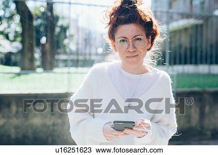 Stock Image - Woman using cellphone on street, Milan, Italy. Fotosearch