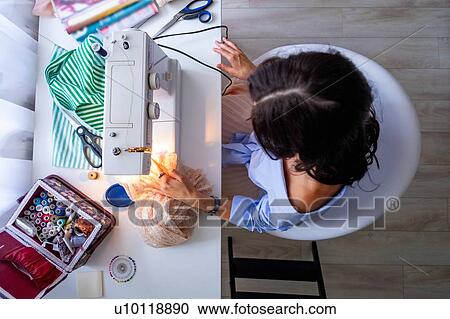 Stock Image - Woman using sewing machine beside window. Fotosearch