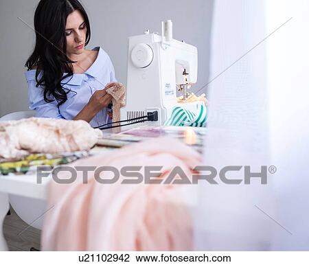 Stock Image - Woman using sewing machine beside window. Fotosearch