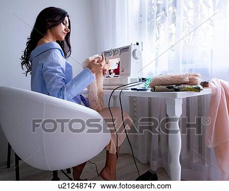 Stock Photo - Woman using sewing machine beside window. Fotosearch