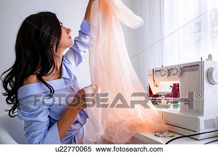 Stock Photography - Woman using sewing machine beside window. Fotosearch