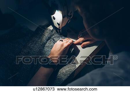 Stock Image - Woman working late at sewing machine. Fotosearch
