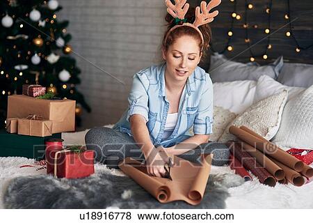 Stock Photo - Woman wrapping Christmas presents on bed. Fotosearch