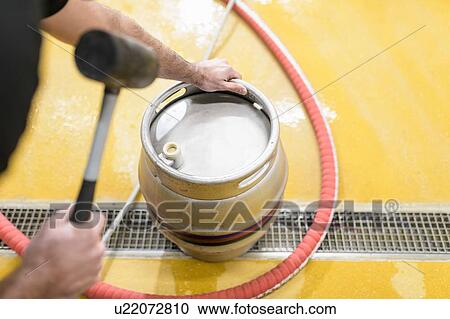 Stock Image - Worker hammering plug into beer barrel in small brewery. Fotosearch