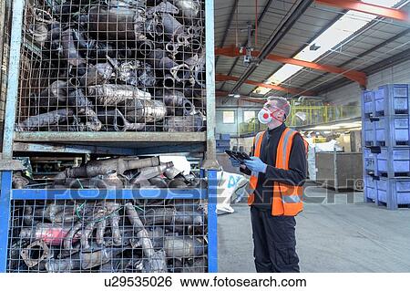 Stock Photograph - Worker inspecting catalytic converters for recycling in recycling factory. Fotosearch