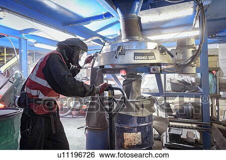 Stock Photograph - Worker sieving recycled metals from catalytic converters in recycling factory. Fotosearch