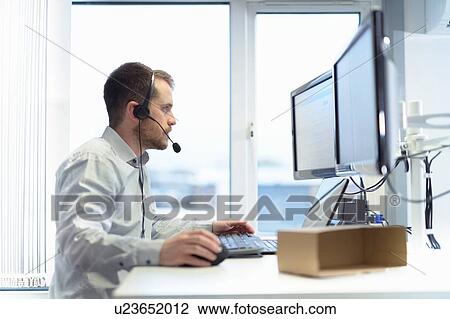 Stock Image - Worker taking customer calls in design department of cardboard box factory. Fotosearch