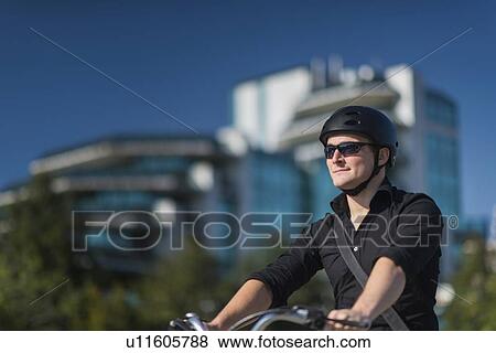 Stock Photo - Young businessman on electric bicycle in business centre. Fotosearch