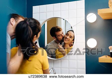 Stock Photo - Young couple kissing in front of wall mirror in bathroom. Fotosearch