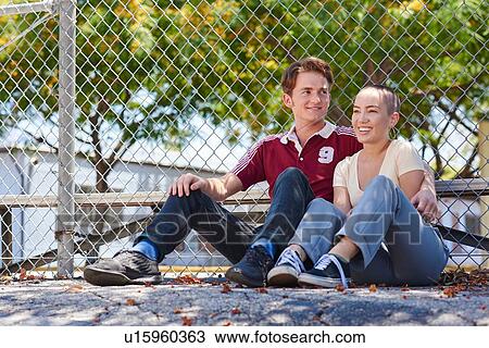 Stock Image - Young couple sitting by park fence, Los Angeles, California, USA. Fotosearch