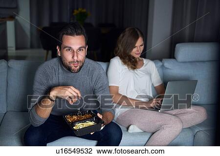 Young couple sitting on sofa in evening eating takeaway and using laptop View Large Photo Image Stock Image - Young couple sitting on sofa in evening eating takeaway and using laptop. Fotosearch