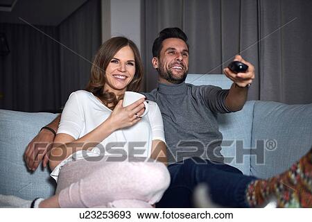 Young couple sitting on sofa in evening watching TV View Large Photo Image Stock Image - Young couple sitting on sofa in evening watching TV. Fotosearch