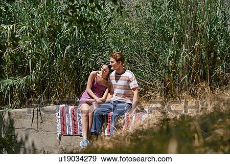Stock Photo - Young couple sitting on wall in park, Los Angeles, California, USA. Fotosearch