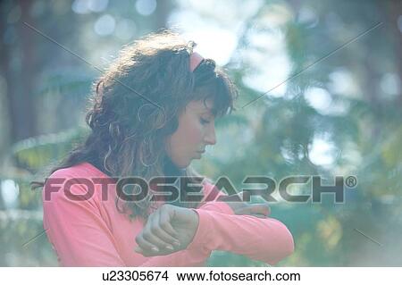 Young female runner putting on armband in sunlit forest View Large Photo Image Picture - Young female runner putting on armband in sunlit forest. Fotosearch