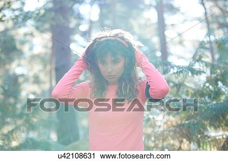 Young female runner putting on headphones in sunlit forest View Large Photo Image Stock Image - Young female runner putting on headphones in sunlit forest. Fotosearch