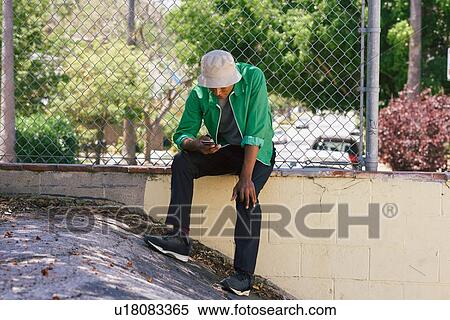 Stock Photography - Young man looking at smartphone by park fence, Los Angeles, California, USA. Fotosearch