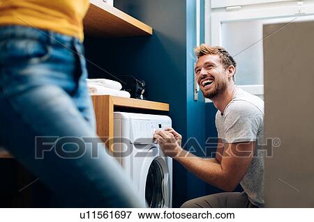 Stock Photo - Young man operating washing machine at home. Fotosearch