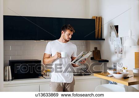 Stock Photo - Young man reading magazine in kitchen. Fotosearch