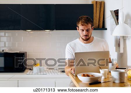 Young man using laptop in kitchen View Large Photo Image Stock Image - Young man using laptop in kitchen. Fotosearch