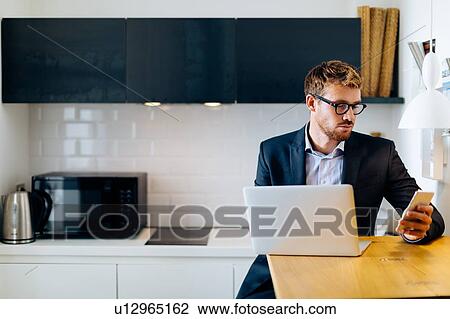 Young man using smartphone and laptop in home office View Large Photo Image Stock Image - Young man using smartphone and laptop in home office. Fotosearch