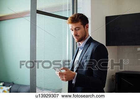 Stock Photo - Young man using smartphone in home office. Fotosearch