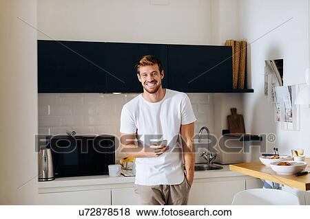 Stock Photo - Young man using smartphone in kitchen. Fotosearch