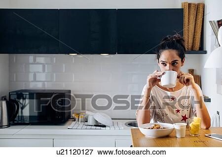 Stock Photo - Young woman drinking coffee in kitchen. Fotosearch