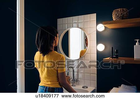 Young woman in front of wall mirror in bathroom View Large Photo Image Stock Photo - Young woman in front of wall mirror in bathroom. Fotosearch