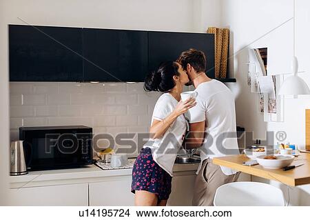 Young woman kissing man's cheek in kitchen View Large Photo Image Picture - Young woman kissing man's cheek in kitchen. Fotosearch