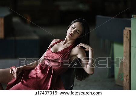 Stock Photograph - Young woman leaning back in chair, exposing thigh. Fotosearch
