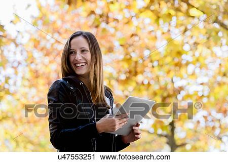 Young woman using digital tablet in park View Large Photo Image Stock Image - Young woman using digital tablet in park. Fotosearch