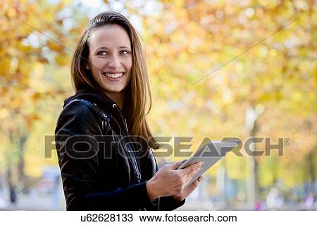 Young woman using digital tablet in park View Large Photo Image Stock Image - Young woman using digital tablet in park. Fotosearch