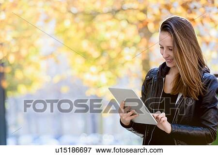Stock Photo - Young woman using digital tablet in park. Fotosearch