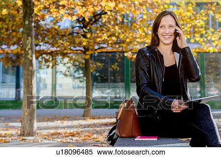 Stock Photography - Young woman using smartphone and digital tablet in park. Fotosearch