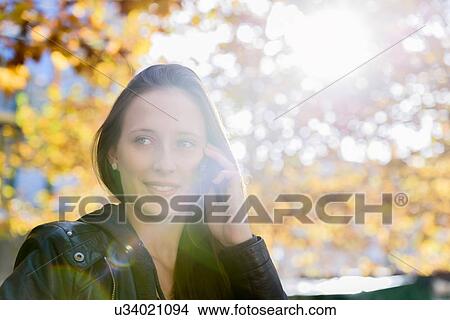 Picture - Young woman using smartphone in park. Fotosearch