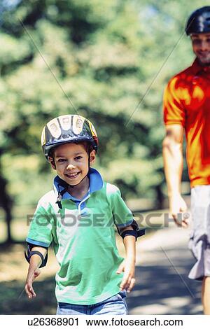 Stock Image - Boy roller skating with father in park. Fotosearch