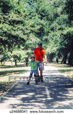 Stock Image - Father and son roller skating in park. Fotosearch