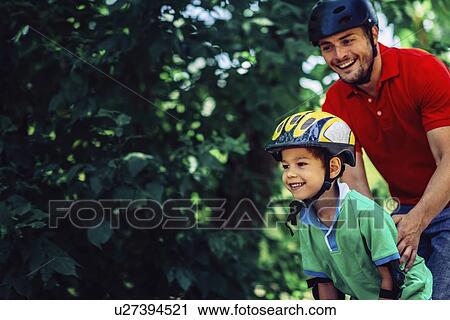 Stock Image - Father teaching son to roller skate in park. Fotosearch