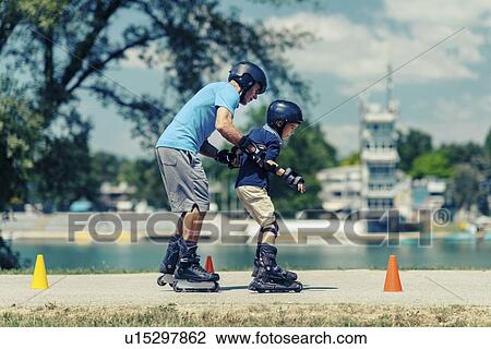 Stock Image - Grandfather teaching grandson to roller skate. Fotosearch