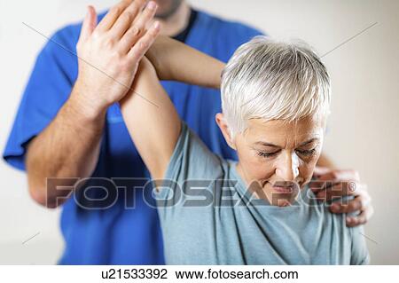 Stock Image - Physical therapist examining patient's shoulder. Fotosearch