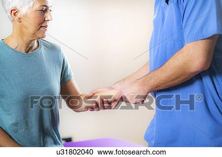 Stock Image - Physical therapist examining patient's wrist. Fotosearch