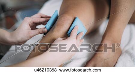 Stock Photo - Placing TENS electrodes on knee. Fotosearch