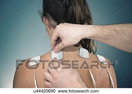 Stock Image - Placing TENS electrodes on shoulders. Fotosearch