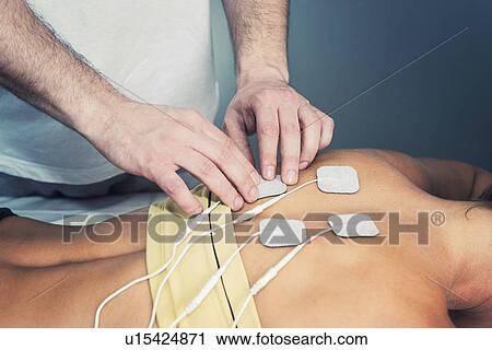 Stock Image - Placing TENS electrodes on upper back. Fotosearch