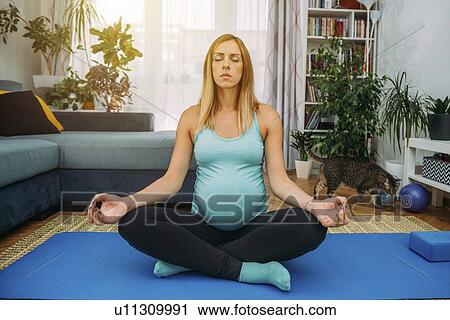 Stock Image - Pregnant woman doing yoga at home. Fotosearch