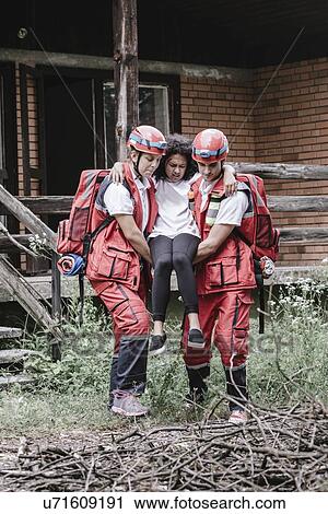 Stock Image - Rescue team evacuating woman from house. Fotosearch
