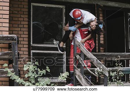 Rescue worker carrying woman out of damaged house View Large Photo Image Stock Photo - Rescue worker carrying woman out of damaged house. Fotosearch
