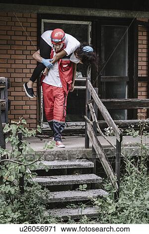 Stock Image - Rescue worker evacuating woman from house. Fotosearch